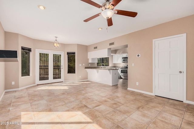 unfurnished living room with visible vents, baseboards, light tile patterned floors, ceiling fan with notable chandelier, and a sink