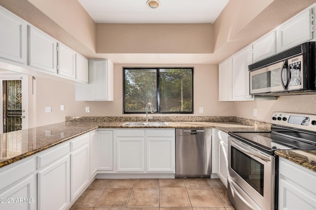 kitchen featuring light tile patterned floors, dark stone counters, a sink, white cabinets, and appliances with stainless steel finishes