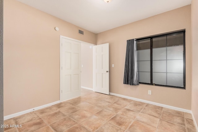 empty room featuring light tile patterned floors, visible vents, and baseboards