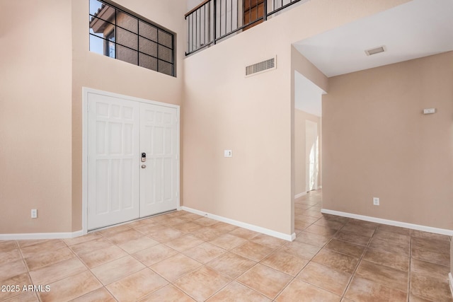 foyer featuring tile patterned flooring, visible vents, a high ceiling, and baseboards