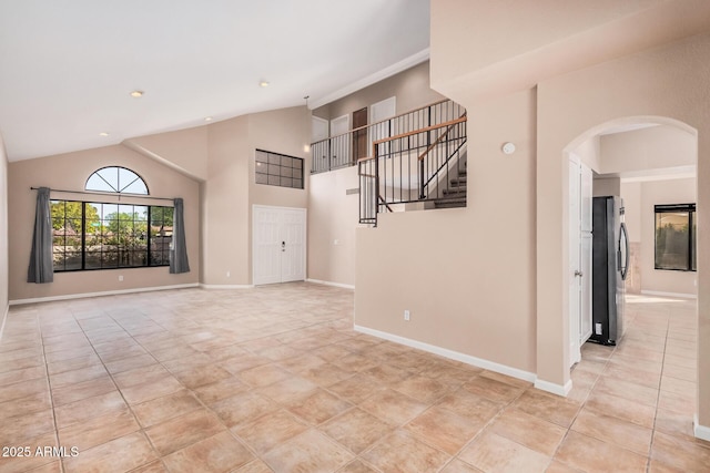 unfurnished living room with baseboards, arched walkways, high vaulted ceiling, and stairs