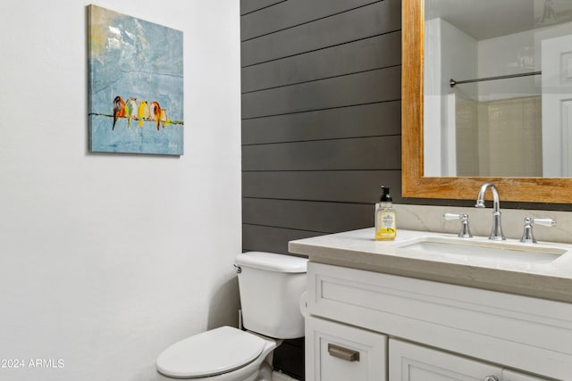 bathroom featuring vanity, walk in shower, toilet, and wood walls