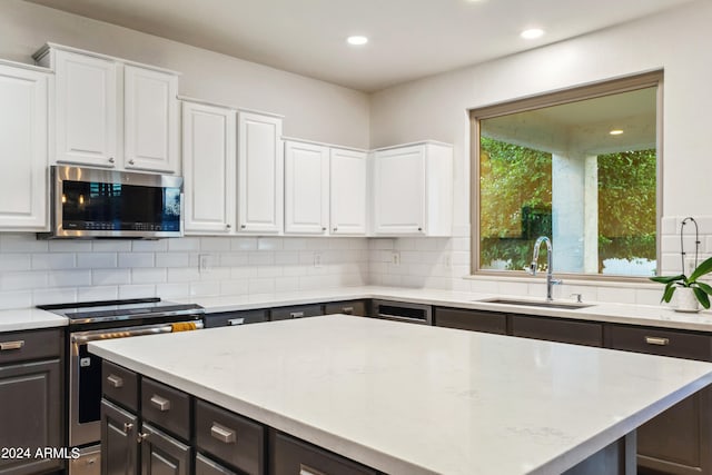 kitchen with sink, backsplash, stainless steel appliances, light stone counters, and white cabinets