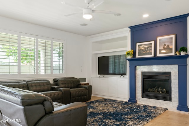 living room with hardwood / wood-style flooring, a tiled fireplace, built in features, and ceiling fan