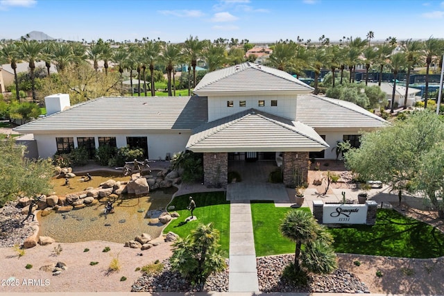 view of front of house with stone siding, a tile roof, a front lawn, and a patio