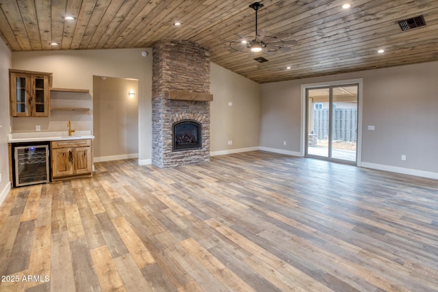 unfurnished living room featuring wine cooler, a stone fireplace, light wood-type flooring, and indoor wet bar