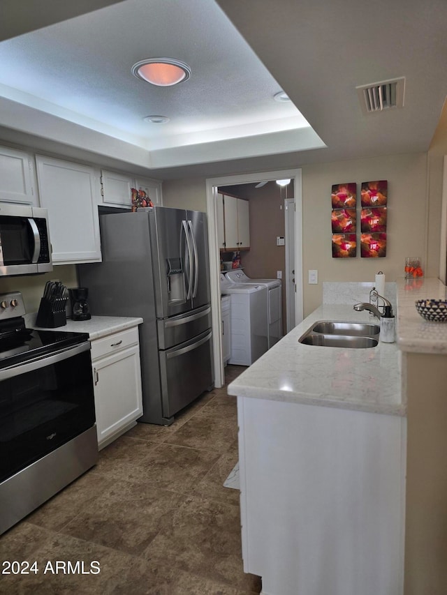 kitchen with stainless steel appliances, a tray ceiling, sink, white cabinets, and washing machine and dryer