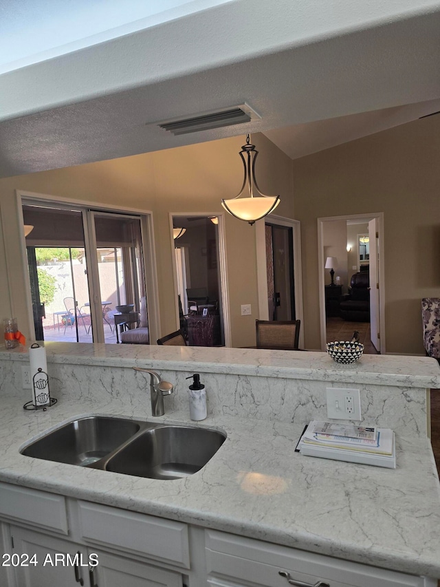 kitchen featuring white cabinets, pendant lighting, light stone countertops, and sink