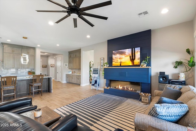 living room with ceiling fan, a large fireplace, and light wood-type flooring