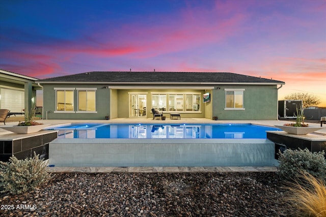 back house at dusk with a swimming pool with hot tub and a patio area