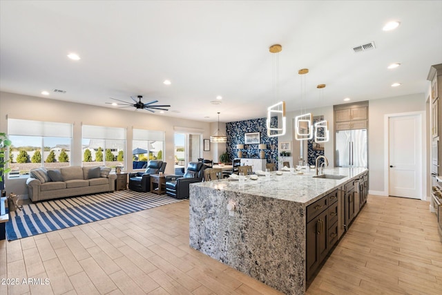 kitchen with ceiling fan, pendant lighting, sink, an island with sink, and built in refrigerator