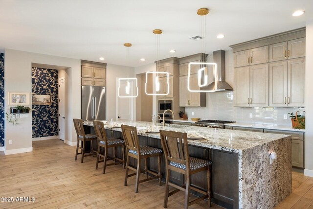 kitchen featuring appliances with stainless steel finishes, wall chimney exhaust hood, decorative light fixtures, sink, and a large island