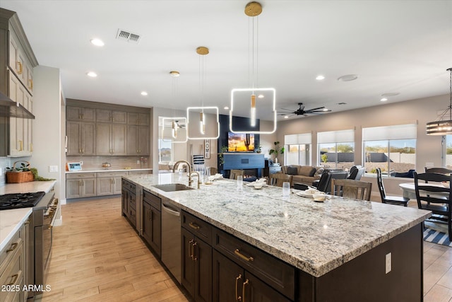 kitchen with a large island with sink, stainless steel appliances, sink, hanging light fixtures, and ceiling fan