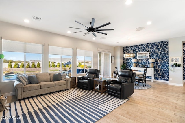 living room featuring a healthy amount of sunlight, ceiling fan with notable chandelier, and light hardwood / wood-style floors