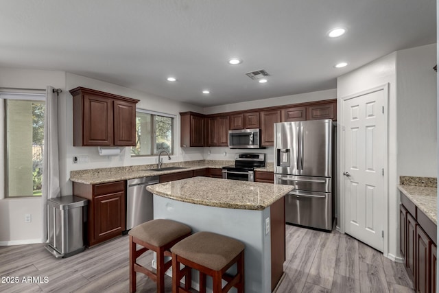 kitchen featuring appliances with stainless steel finishes, light stone counters, a kitchen island, sink, and light hardwood / wood-style flooring