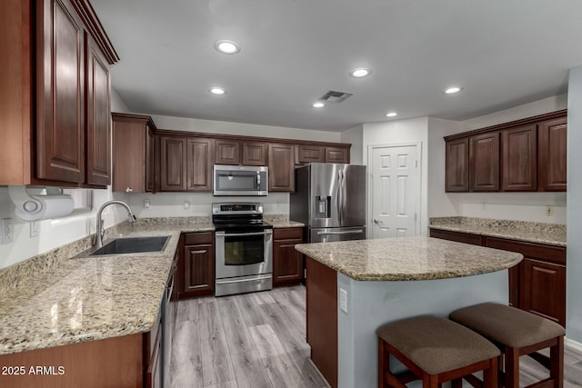 kitchen with light hardwood / wood-style floors, stainless steel appliances, a center island, light stone counters, and sink