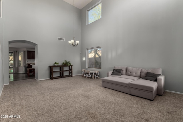 carpeted living room featuring plenty of natural light, a towering ceiling, and a chandelier