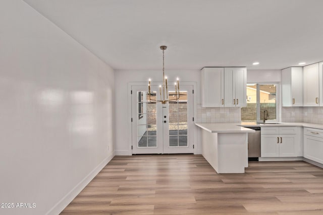 kitchen with a sink, white cabinetry, dishwasher, decorative backsplash, and an inviting chandelier