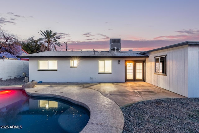 back of house at dusk with a patio area, roof with shingles, a fenced in pool, concrete block siding, and central AC unit
