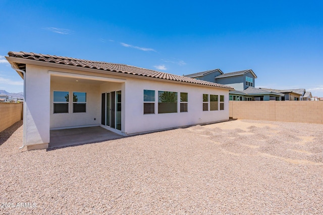 rear view of house with a patio area, stucco siding, a tiled roof, and a fenced backyard