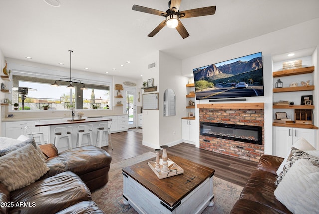 living room with visible vents, a brick fireplace, baseboards, a ceiling fan, and dark wood-style floors