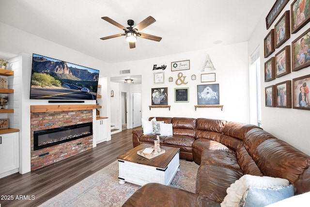 living area with visible vents, wood finished floors, a glass covered fireplace, and a ceiling fan