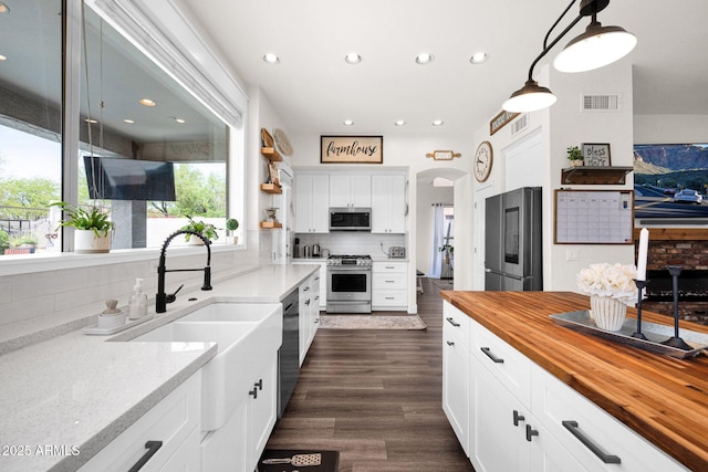 kitchen with backsplash, white cabinetry, butcher block countertops, stainless steel appliances, and visible vents