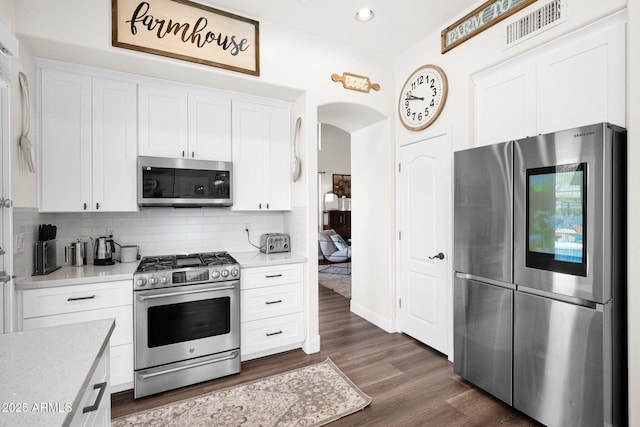 kitchen featuring light countertops, stainless steel appliances, decorative backsplash, dark wood-style floors, and visible vents