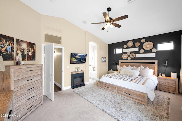 bedroom with ensuite bathroom, carpet, arched walkways, a glass covered fireplace, and vaulted ceiling