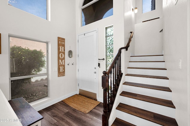 foyer entrance with stairs, wood finished floors, a towering ceiling, and baseboards