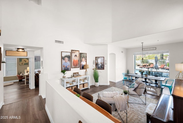 living room with arched walkways, a towering ceiling, visible vents, and dark wood finished floors