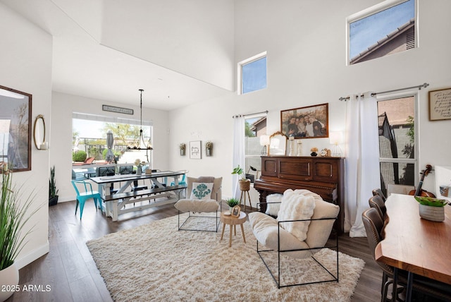 living room with baseboards, wood finished floors, a towering ceiling, and an inviting chandelier