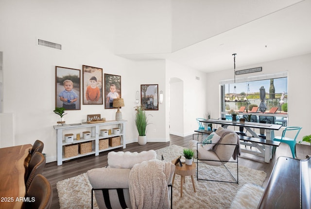 living area featuring baseboards, a high ceiling, arched walkways, visible vents, and wood finished floors