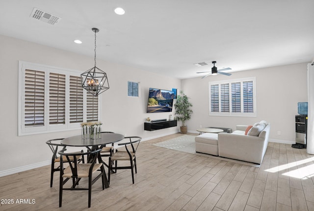 dining space with ceiling fan with notable chandelier and light hardwood / wood-style floors