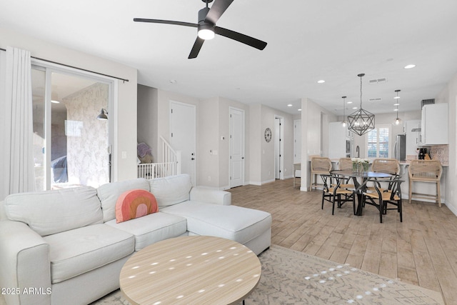 living room featuring ceiling fan with notable chandelier and light wood-type flooring