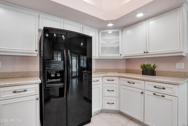 kitchen with light tile patterned floors, light stone countertops, black refrigerator with ice dispenser, and white cabinets