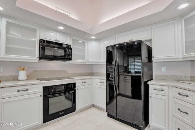 kitchen featuring white cabinets, light tile patterned floors, black appliances, a raised ceiling, and light stone countertops