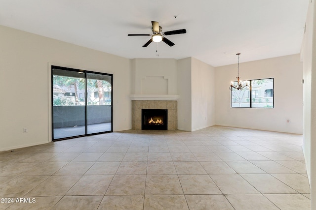 unfurnished living room featuring a tile fireplace, a wealth of natural light, light tile patterned floors, and ceiling fan with notable chandelier