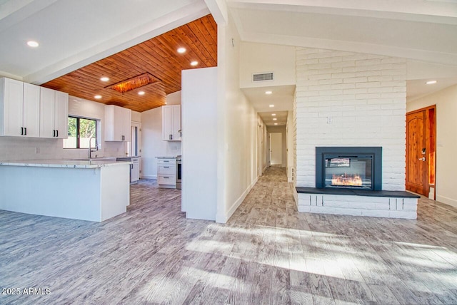 21 Hummingbird Cir, Sedona, AZ 86336 - kitchen featuring lofted ceiling, white cabinets, light wood-style floors, a sink, and a brick fireplace