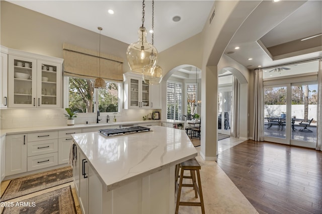 kitchen featuring a kitchen island, pendant lighting, sink, white cabinets, and light stone counters