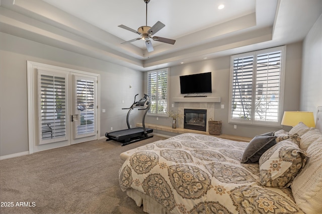 bedroom with a tile fireplace, carpet flooring, access to exterior, ceiling fan, and a raised ceiling