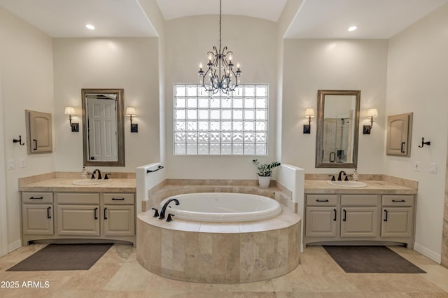 bathroom with an inviting chandelier, vanity, and tiled bath