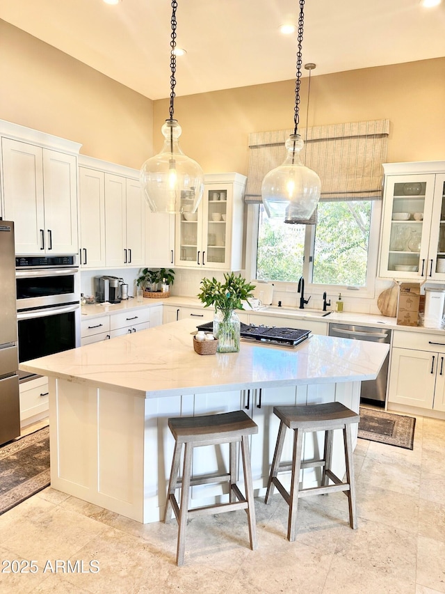 kitchen featuring appliances with stainless steel finishes, hanging light fixtures, a kitchen breakfast bar, white cabinets, and a kitchen island