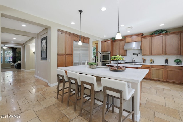 kitchen with decorative backsplash, stainless steel appliances, a breakfast bar, hanging light fixtures, and a center island with sink