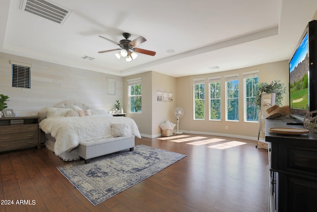 bedroom with ceiling fan, a tray ceiling, dark hardwood / wood-style flooring, and multiple windows