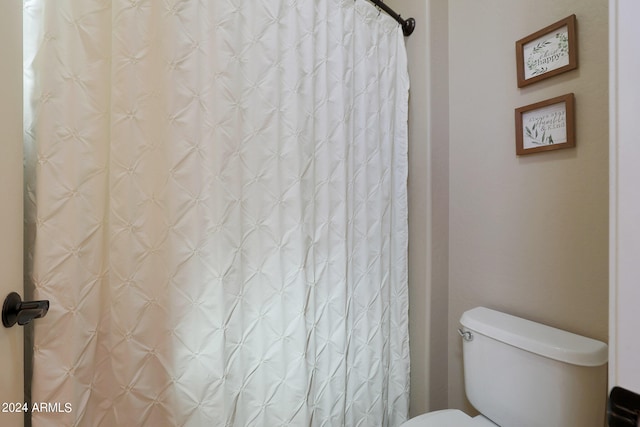 bathroom featuring toilet and curtained shower