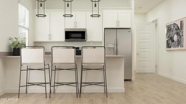 kitchen featuring stainless steel refrigerator with ice dispenser, a kitchen breakfast bar, white cabinetry, and hanging light fixtures