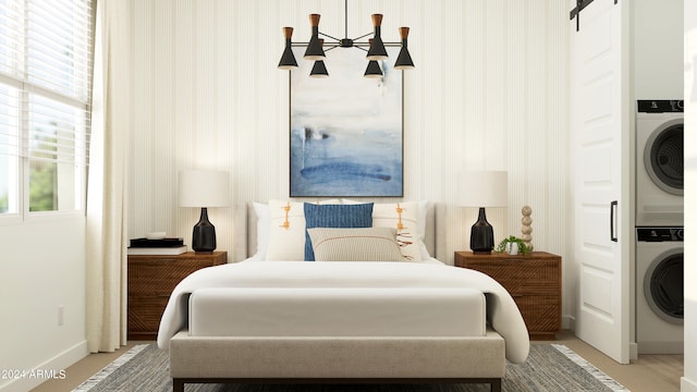 bedroom featuring stacked washer / dryer, a barn door, and a notable chandelier