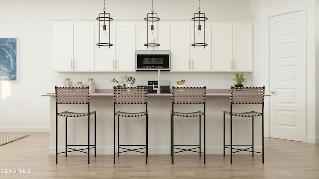 kitchen with a kitchen bar, white cabinets, hanging light fixtures, and a kitchen island with sink