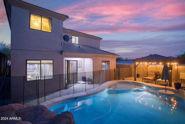 pool at dusk featuring a gazebo and a patio